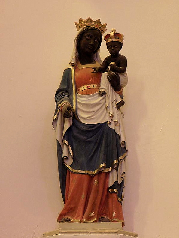 Statue of a dark-skinned, crowned Madonna and Child in blue, white, and orange robes, mounted on a wall pedestal.