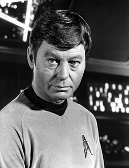 A black-and-white publicity portrait of Dr. Leonard McCoy (actor DeForest Kelley) in his Starfleet uniform.
