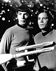 A black-and-white publicity photo of Spock and Captain Kirk standing side by side in Starfleet uniforms, with a model of the USS Enterprise displayed in front of them.