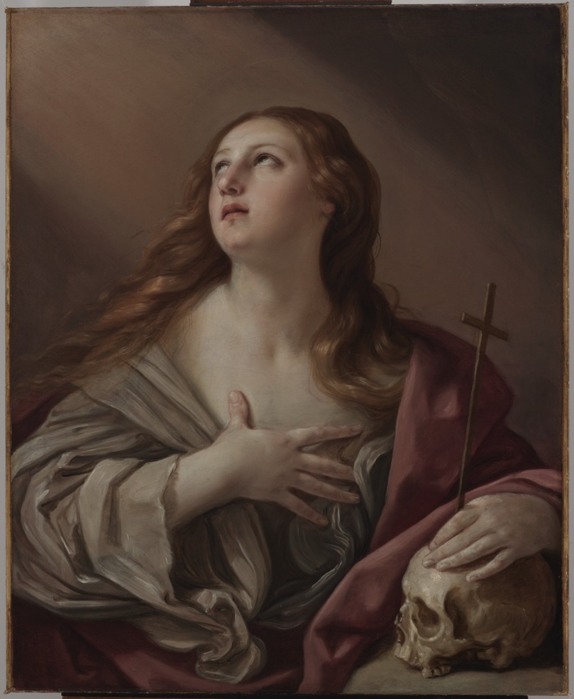 A half-length painting of a woman with long auburn hair gazing upward, one hand pressed to her bare chest and the other resting on a human skull beside a small wooden cross, draped in a rose-colored cloak.