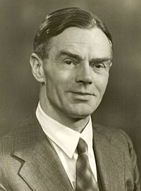 Black-and-white studio headshot of an unidentified middle-aged man with neatly combed, side-parted hair, wearing a dark suit jacket, white shirt, and patterned tie, photographed from the chest up against a plain background (no caption identifies the sitter).