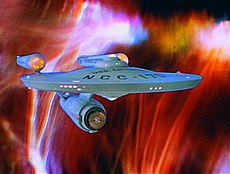 A color image of the USS Enterprise starship, its saucer section and registry markings visible, set against a fiery orange-red background.
